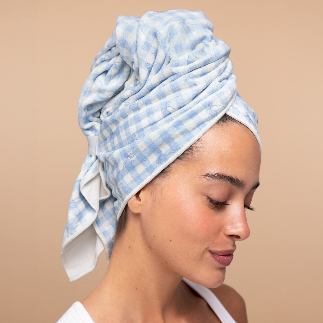 Model with wet hair twisted up in the Kitsch XL Hair Towel Wrap in blue gingham print, secured with the elastic strap after showering